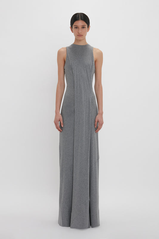 A person stands facing the camera, wearing a Victoria Beckham Frame Detailed Maxi Dress In Titanium with a high neckline, creating an elongated silhouette. The background is plain white.