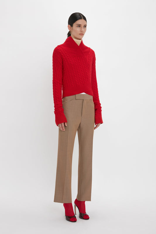 A person stands against a plain background, wearing a red sweater, Wide Cropped Flare Trouser In Tobacco by Victoria Beckham that offer a flattering hint of ankle, and red open-toe heels. Their hands are loosely at their sides.