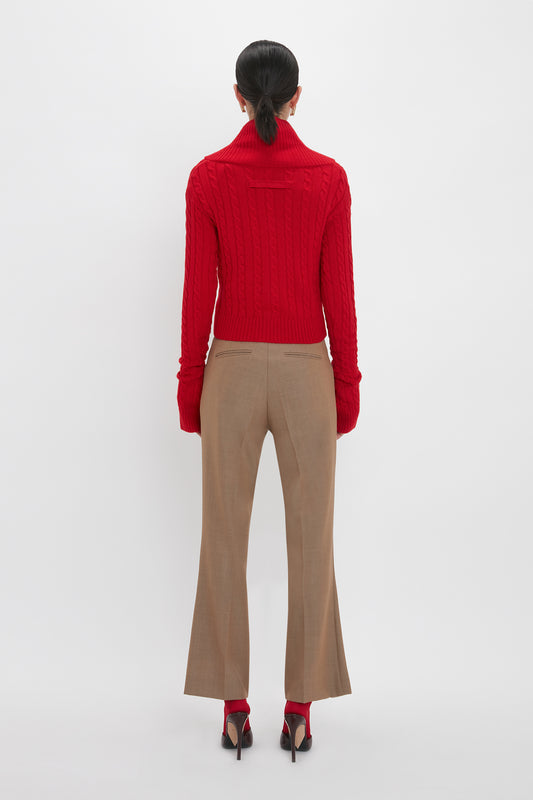 A person stands with their back to the camera, wearing a Wrap Detail Jumper In Red from the Victoria Beckham brand, beige pants, and red shoes with heels. Their hair is tied back in a low ponytail. The luxury knitwear piece contrasts beautifully against the plain white background.