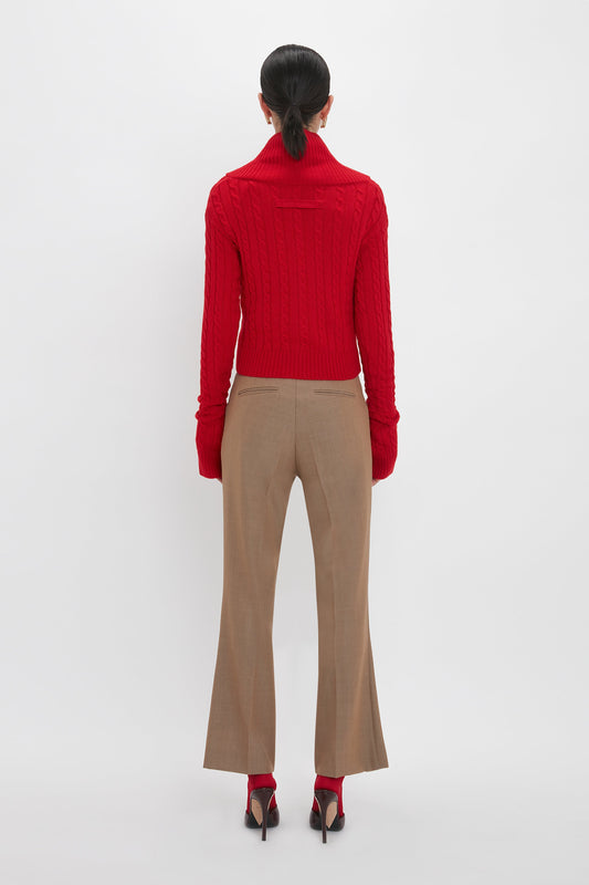 A person is standing with their back to the camera, wearing a red turtleneck sweater, Wide Cropped Flare Trouser In Tobacco by Victoria Beckham that adds a flattering hint of ankle, and red heels, with their hair tied back.