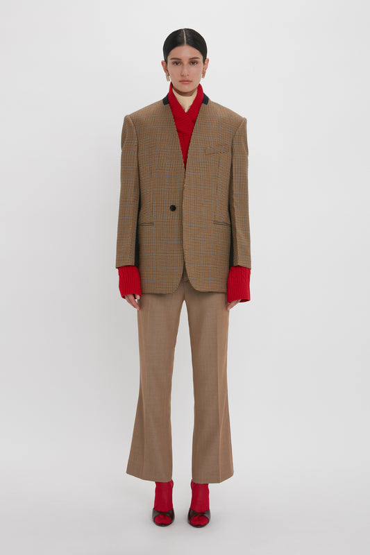 A person stands against a white background wearing a Victoria Beckham Pocket Detail Collarless Jacket In Tobacco, matching wide-legged trousers, a red turtleneck sweater, and red shoes.