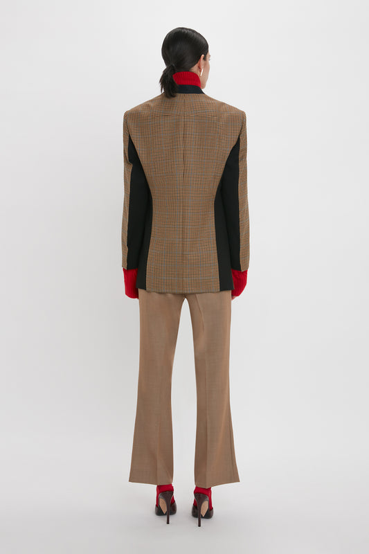 A person with long hair, seen from the back, is clad in a Pocket Detail Collarless Jacket In Tobacco by Victoria Beckham featuring a modern oversized fit, beige trousers, red gloves, and matching high heels, all set against a plain white background.