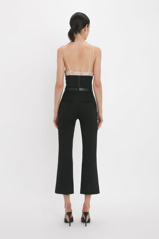 A person with dark hair in a ponytail is wearing a Victoria Beckham Lace Detail Cami Top In Black, featuring a deep-V neckline and black high-heeled shoes, seen from the back against a plain white background.