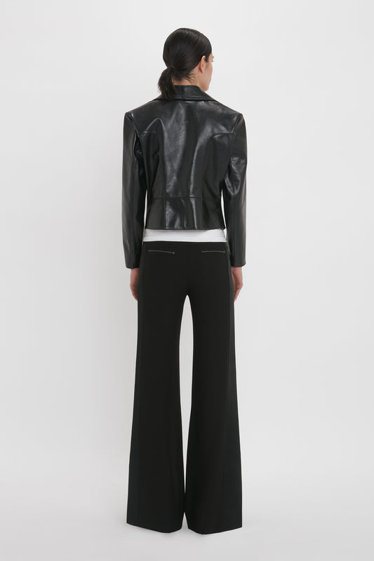 A person with dark hair, facing away from the camera, is wearing a Victoria Beckham Tailored Leather Biker Jacket In Black and black wide-leg pants against a plain white background—a modern classic look.