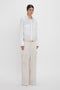 Person standing against a white background, wearing the Oversized Pocket Shirt In White by Victoria Beckham made from organic cotton and beige wide-leg cargo pants with a belt, showcasing modern sophistication.