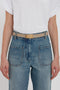 Person wearing a white t-shirt tucked into blue high-waisted jeans with large front pockets, accessorized with a Victoria Beckham Exclusive Frame Belt In Beige Leather.