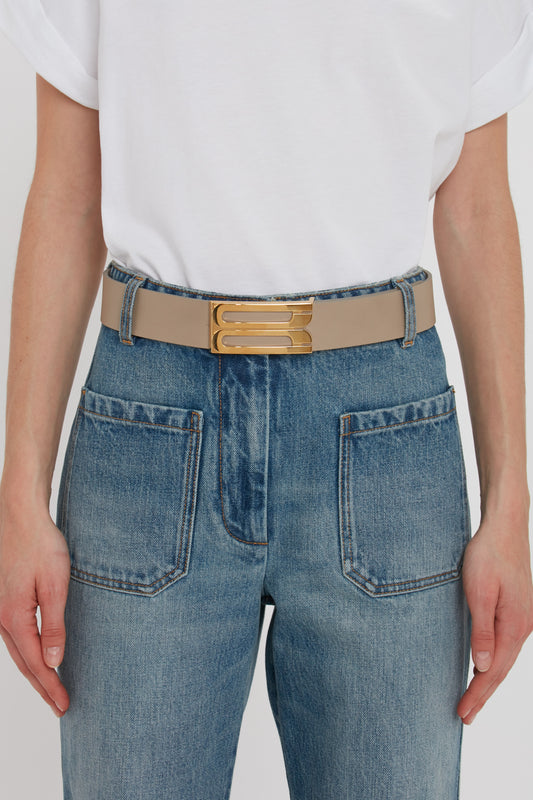 Close-up of a person wearing blue jeans with a Victoria Beckham Exclusive Jumbo Frame Belt in Beige Leather, focusing on the gold hardware and back pockets.
