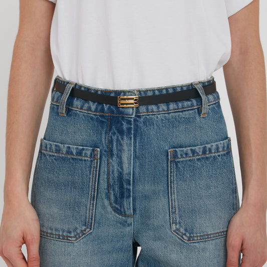 Close-up of a person wearing blue jeans with a detailed view of a gold buckle on a Victoria Beckham Exclusive Micro Frame Belt In Black Leather.
