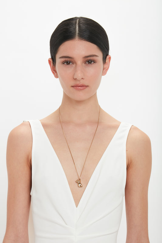 A woman with dark hair wearing a white sleeveless top and a long, light gold Exclusive Body Charm Necklace In Light Gold by Victoria Beckham, gazes directly at the camera against a plain background.