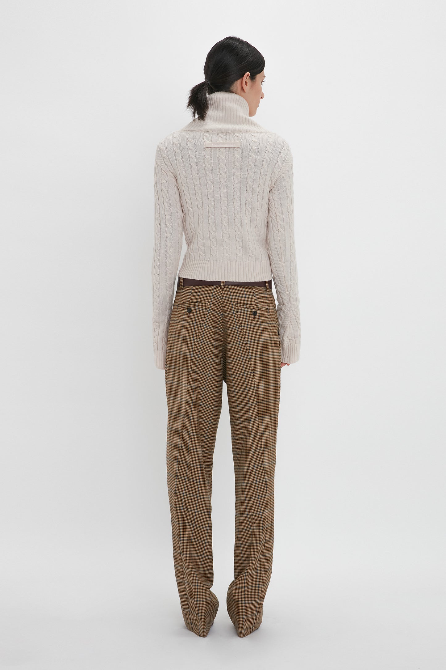 A person wearing a Victoria Beckham Wrap Detail Jumper In Bone and plaid trousers, facing away from the camera, stands against a plain white background.