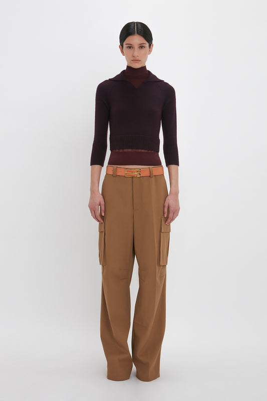 A person stands against a plain white background wearing a Victoria Beckham Double Layer Top In Deep Mahogany and tan cargo pants with a belt.