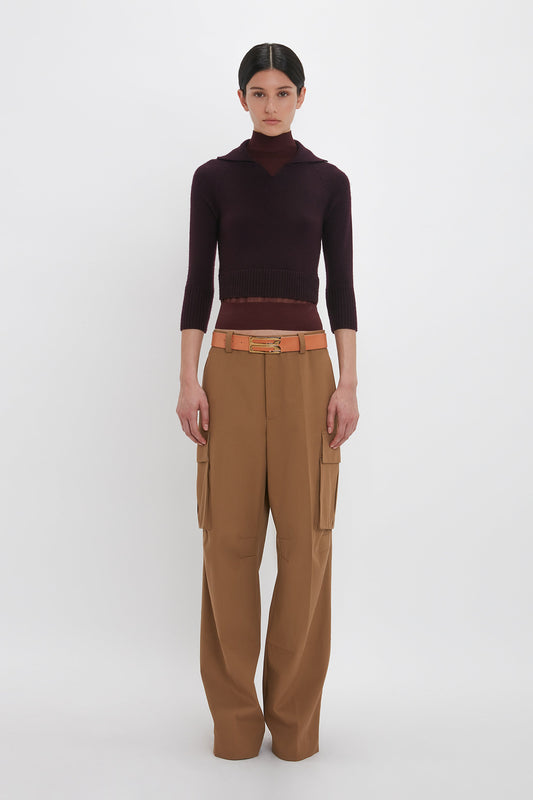 A person with a neutral expression is wearing a dark long-sleeve top and Relaxed Cargo Trouser In Tobacco by Victoria Beckham with a tan belt, standing against a plain white background. The outfit showcases a relaxed silhouette, perfect for everyday wear.
