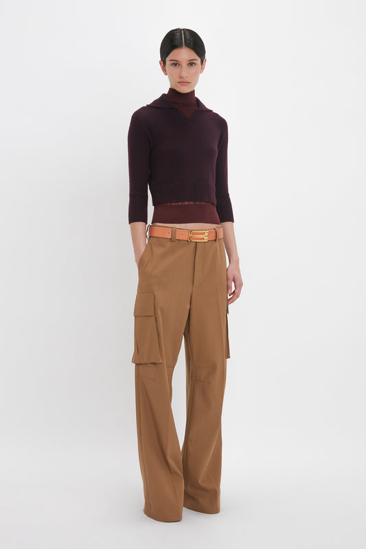 A person stands against a white background, wearing a Victoria Beckham Double Layer Top In Deep Mahogany and tan wide-leg cargo pants with a tan belt.