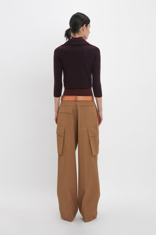 Person wearing a dark Victoria Beckham Double Layer Top In Deep Mahogany and tan utility pants with large pockets, standing and facing away from the camera against a white background.