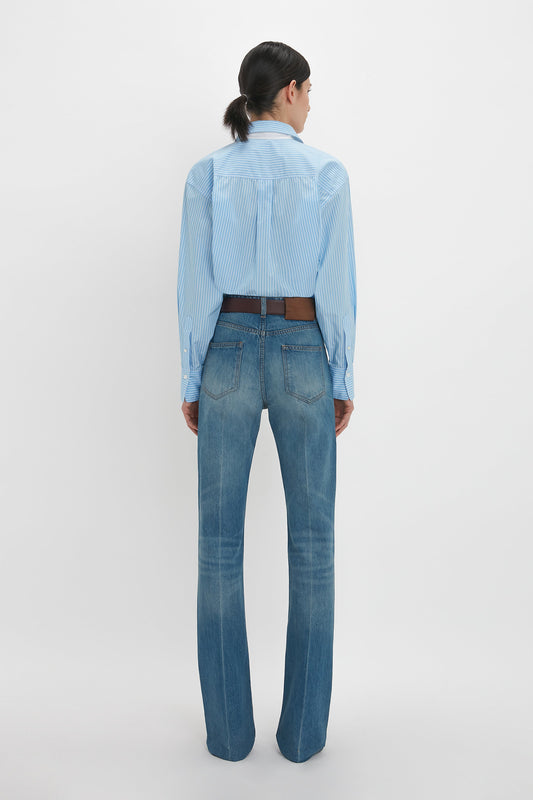 A person with dark hair is seen from the back, wearing a Cropped Long Sleeve Shirt In Marina-White by Victoria Beckham tucked into blue jeans with a brown belt.