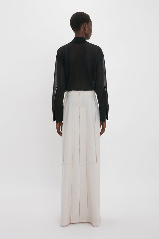 Person standing with back to the camera, wearing a Victoria Beckham Pocket Detail Shirt In Black with a collared neckline and high-waisted beige wide-leg pants.