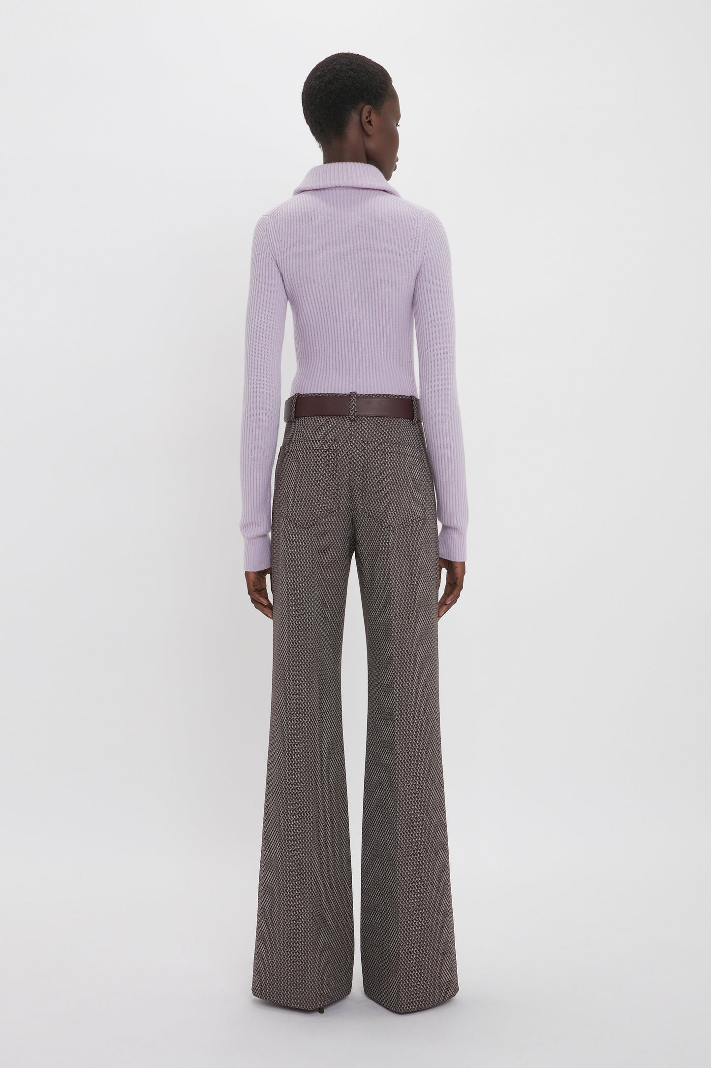 Person stands against a white backdrop facing away, wearing a lavender turtleneck sweater and Victoria Beckham Alina Trouser In Tobacco.