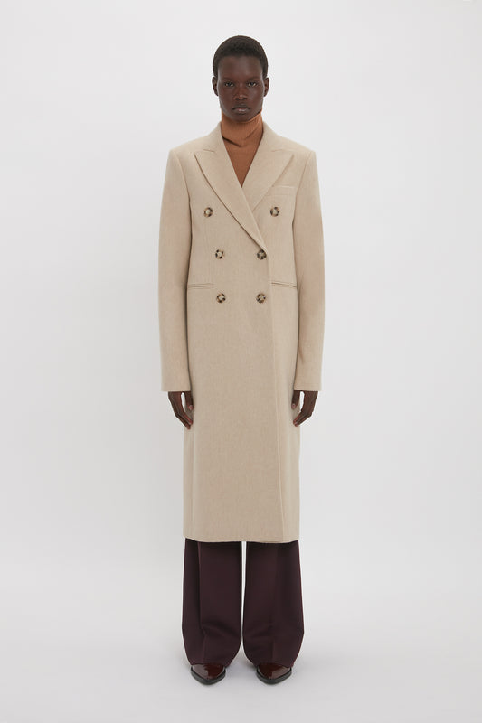A person stands facing forward wearing the Victoria Beckham Tailored Slim Coat In Bone, a brown turtleneck, and dark wide-leg trousers against a plain white background.