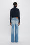 Rear view of a person with short hair wearing a navy turtleneck sweater and stylish tailored Alina High Waisted Jean In Light Summer Wash by Victoria Beckham against a plain white background, exuding an understated elegance reminiscent of Victoria Beckham's fashion.