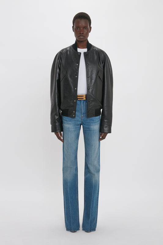 Person wearing a Victoria Beckham Leather Varsity Jacket In Black over a white shirt, blue jeans, and black shoes, standing against a white background.