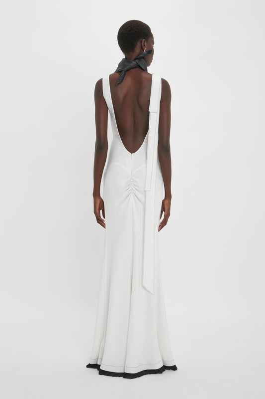 A person is wearing the Victoria Beckham Exclusive V-Neck Gathered Waist Floor-Length Gown In Ivory, standing against a plain white background. The hourglass silhouette of the dress features a gathered section at the lower back.