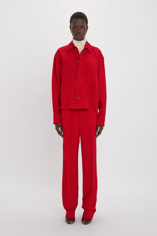 A person stands against a plain background wearing a Cropped Long Sleeve Shirt In Carmine by Victoria Beckham and matching red pants with a white turtleneck underneath, evoking an effortlessly chic vibe reminiscent of Victoria Beckham monogram styles.