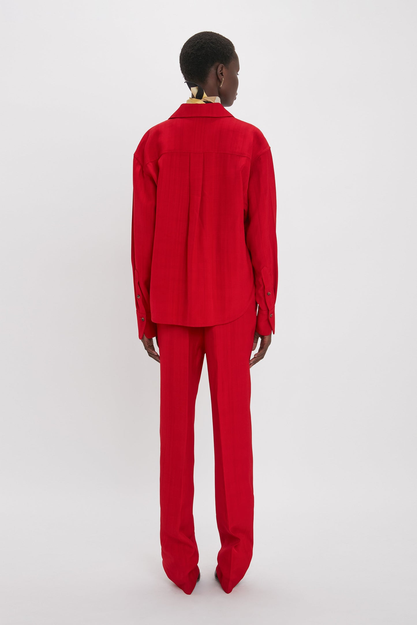 A person is standing against a plain background wearing a carmine long-sleeve shirt and matching Tapered Leg Trouser In Carmine by Victoria Beckham, facing away from the camera.