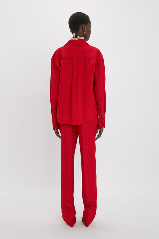 Person standing with back to the camera, wearing a Cropped Long Sleeve Shirt In Carmine from Victoria Beckham, matching red pants, and red pointed shoes against a white background.
