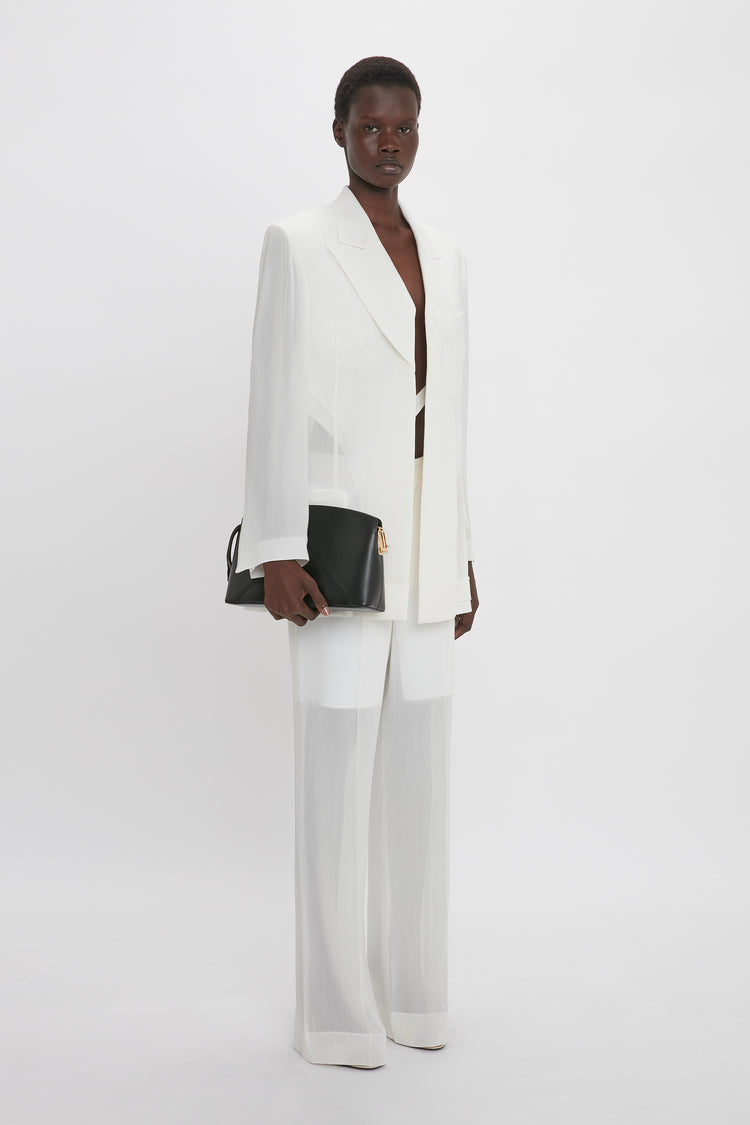 Person modeling a white pantsuit with wide-legged trousers, featuring the Fold Detail Tailored Jacket In White by Victoria Beckham for modern flair. They are holding a black clutch bag and standing against a plain white background.