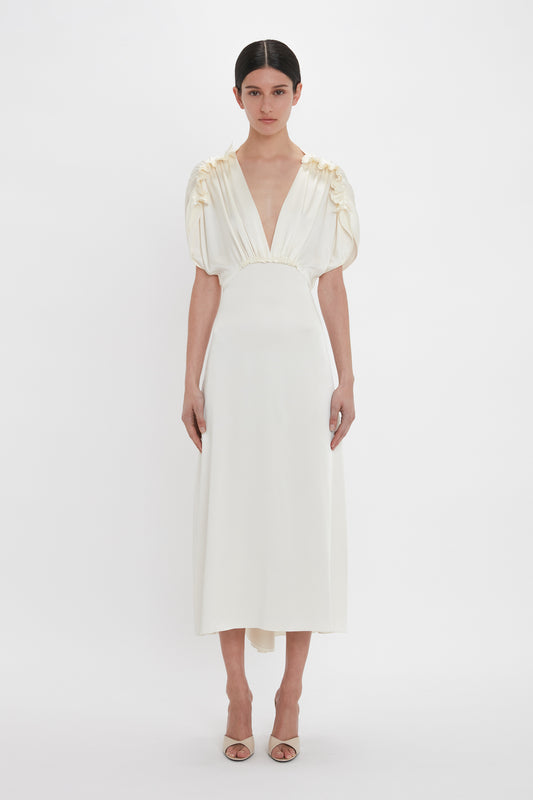 A person wearing a Victoria Beckham Exclusive V-Neck Ruffle Midi Dress In Ivory stands against a plain white background.