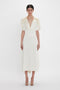 A person wearing a Victoria Beckham Exclusive V-Neck Ruffle Midi Dress In Ivory stands against a plain white background.