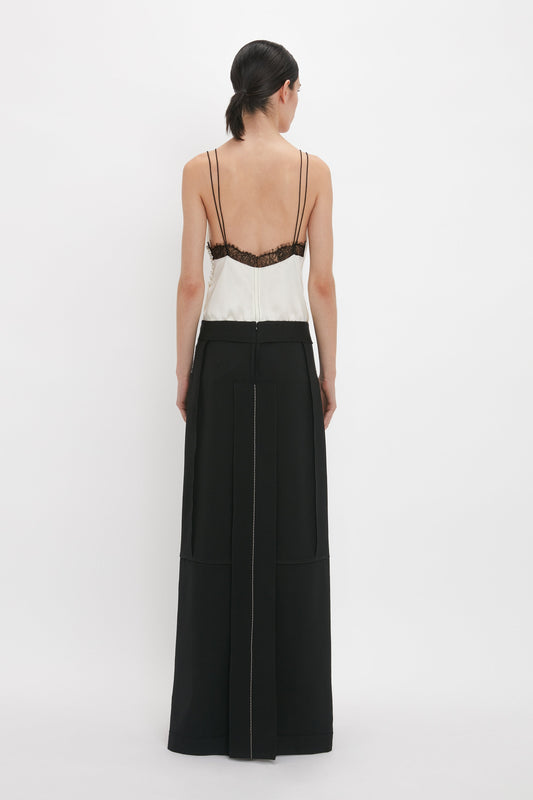 Person standing facing away from the camera, wearing a Victoria Beckham Lace Detail Cami Top In Harvest Ivory with thin straps, paired with black wide-leg pants featuring a straight seam down the back.