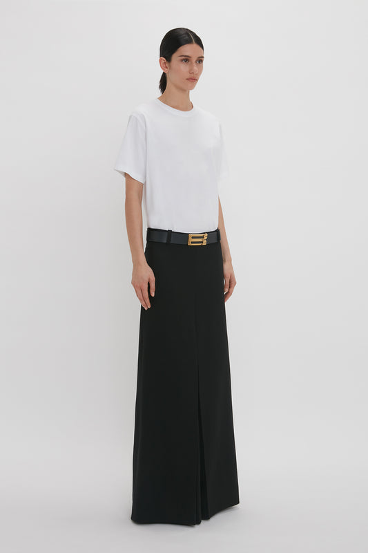 A woman in a white t-shirt and floor-length box pleat skirt in black from Victoria Beckham stands against a plain white background.