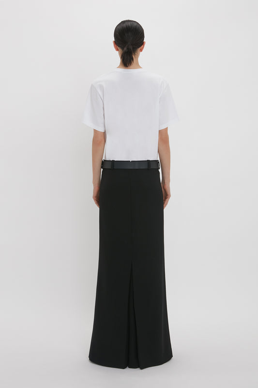 Woman viewed from behind wearing a white t-shirt and Floor-Length Box Pleat Skirt In Black by Victoria Beckham against a plain background.