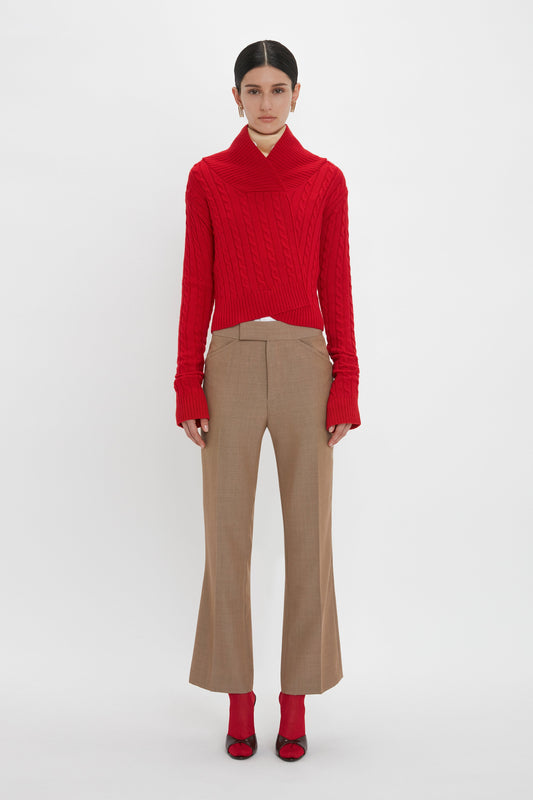 Person standing against a white background, wearing a red knit sweater, Victoria Beckham Wide Cropped Flare Trouser In Tobacco, red socks, and red shoes. Hair is styled neatly back.