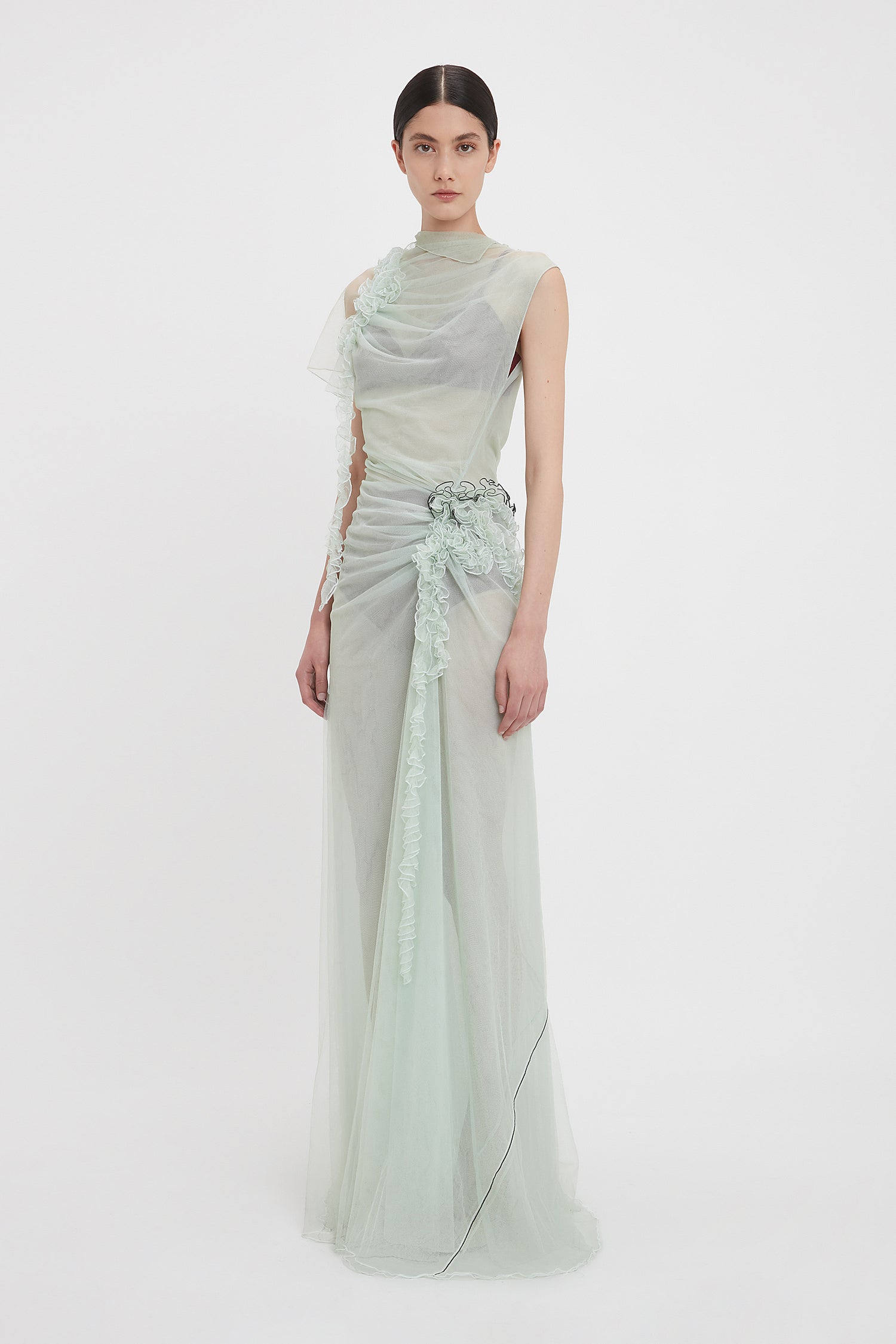 Person wearing a sleeveless, ethereal Gathered Tulle Detail Floor-Length Dress In Jade by Victoria Beckham, with ruched detailing and lace accents on a white background.
