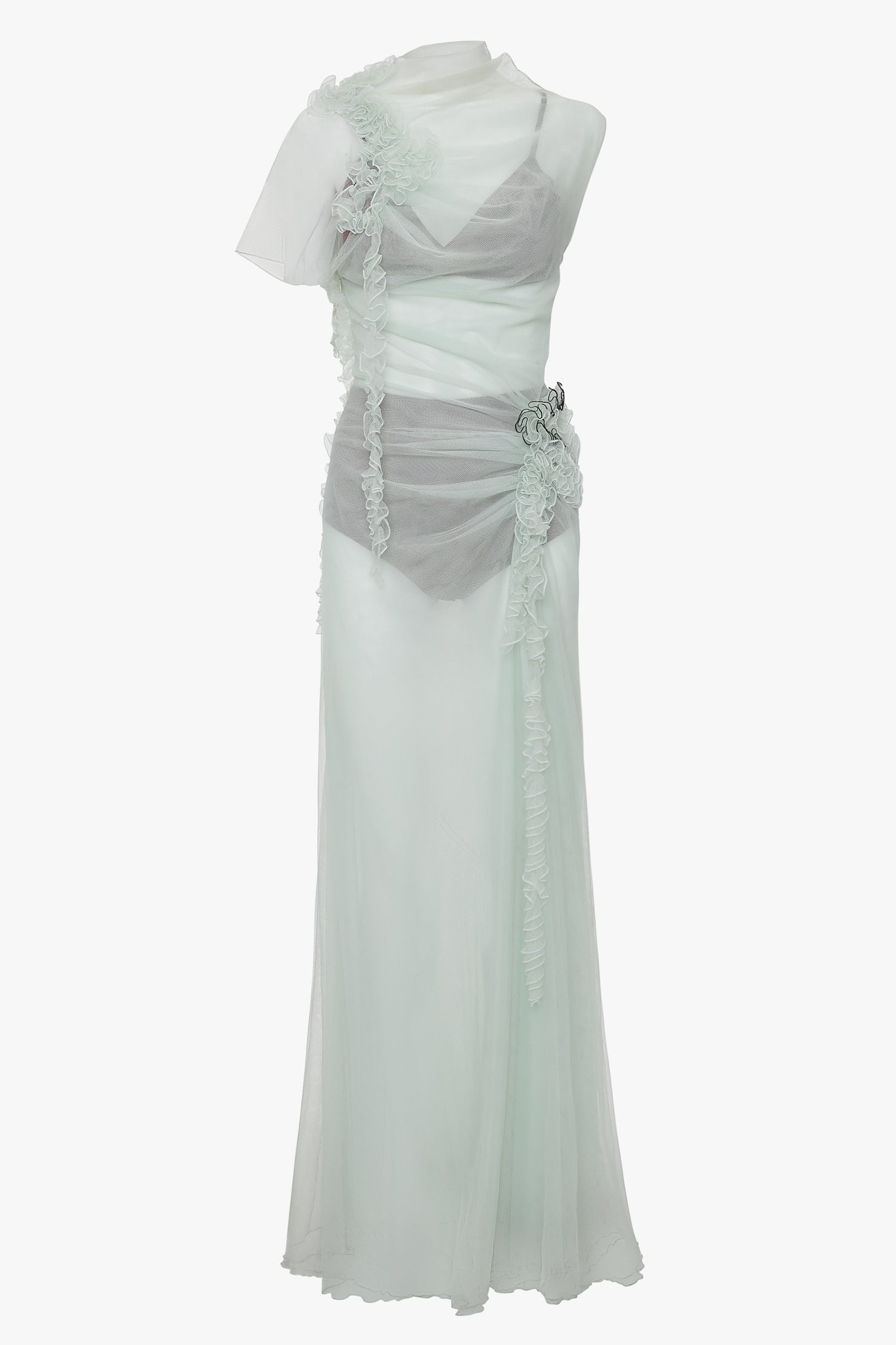 A Gathered Tulle Detail Floor-Length Dress In Jade with delicate ruffles and sheer fabric overlaying a slip, featuring asymmetrical design elements and a decorative floral accent at the waist. This ethereal gown can be found on VictoriaBeckham.com.