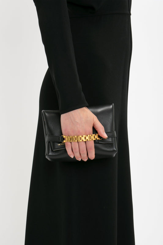 A person in a Dolman Midi Dress in Black by Victoria Beckham holding a small black leather chain pouch with a gold chain detail.
