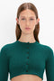 A person with long brown hair is wearing a VB Body Cropped Cardi In Lurex Green by Victoria Beckham, featuring scalloped detailing and a form-fitting silhouette, as they pose against a plain white background.