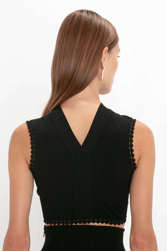 A person with long, straight hair wearing the versatile VB Body Scallop Trim Tank Top In Black by Victoria Beckham is shown from behind against a plain white background—a true summer essential.