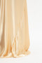 Close-up of a portion of a flowing, silky, Exclusive Floor-Length Cami Dress In Gold by Victoria Beckham draped elegantly against a white background, evoking a 1990s-inspired aesthetic.