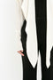 A person wearing a black outfit with a long white, cape-style drape hanging down the front. The image only shows from the neck to mid-thigh, featuring the Oversized Bow Detail Blouse In Vanilla by Victoria Beckham.