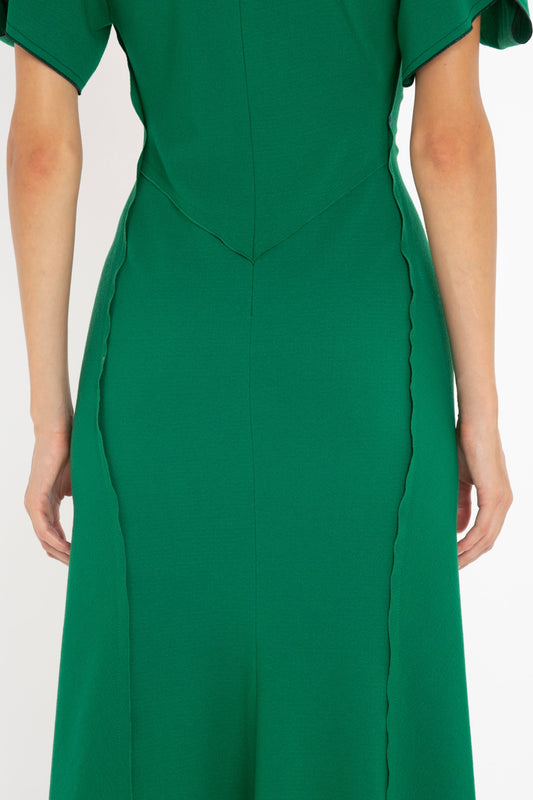 Close-up of a woman wearing a Victoria Beckham Gathered V-Neck Midi Dress in Emerald with a fitted bodice, scalloped trim, and mid-length sleeves.