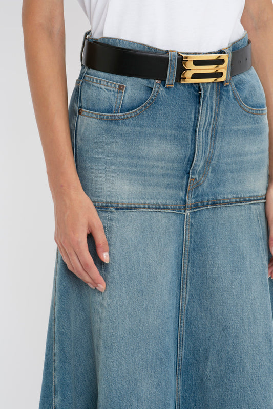 Person wearing a Victoria Beckham Patched Denim Skirt In Vintage Wash with visible seams and a raw edge hem, paired with a white t-shirt and a black belt featuring a gold buckle. Only the lower torso and upper thigh area are visible in the image.