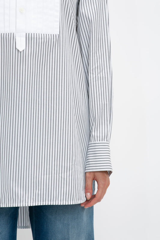 A person wearing a long-sleeved, vertically striped Tuxedo Bib Shirt in Black and Off-White from Victoria Beckham and blue jeans, with their arm hanging at their side.