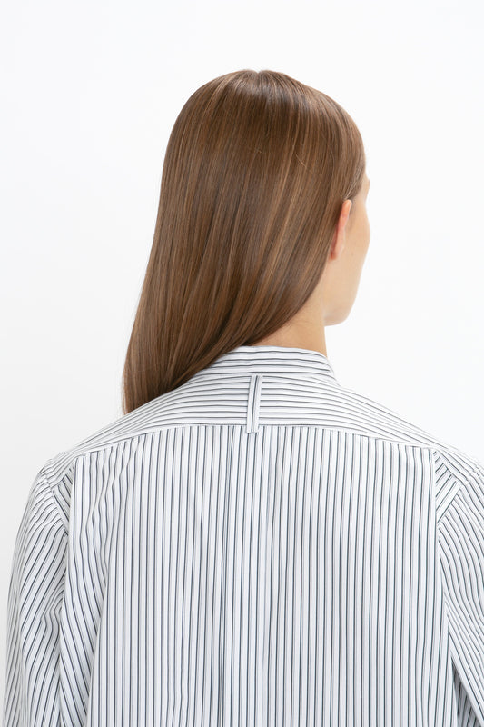 A person with long, straight brown hair is shown from the back, wearing a Tuxedo Bib Shirt in Black and Off-White by Victoria Beckham that adds a modern touch to traditional menswear silhouettes.