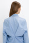 A person with straight brown hair is seen from behind, wearing a light blue Pleat Detail Raglan Shirt In Oxford Blue by Victoria Beckham with a gathered design at the back and a contemporary silhouette.