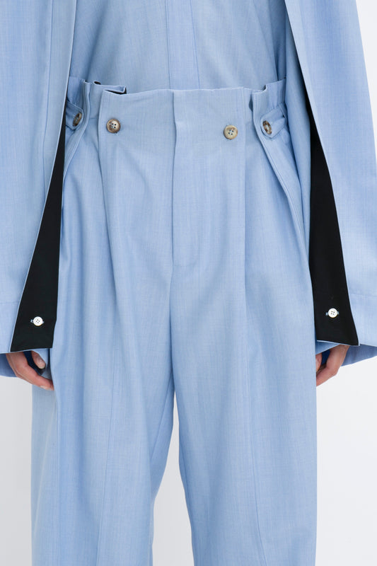 Close-up of a person wearing Victoria Beckham Gathered Waist Utility Trouser In Oxford Blue with button details and a matching jacket featuring black accents inside the cuffs, showcasing a blend of utility wear and style.