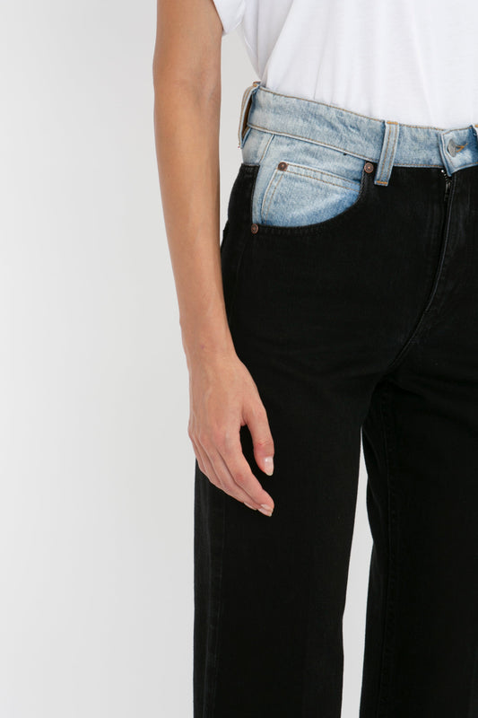 Close-up of a person wearing a white t-shirt tucked into Victoria Beckham's Julia Jean In Contrast Wash with a blue denim waistband, seen from the waist down. Hand resting casually by their side.