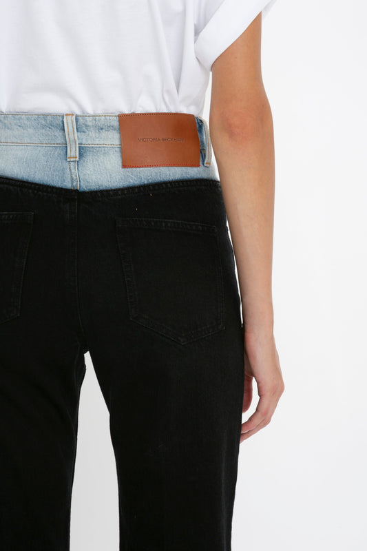 Close-up of a person wearing black high waist Julia Jeans In Contrast Wash with a white t-shirt tucked in, featuring a brown Victoria Beckham brand patch on the back.